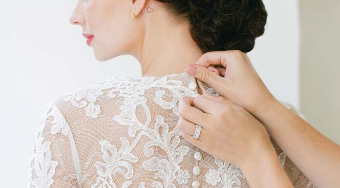 Top Tips for Top-Notch Bridal Alterations buttoning up a long sleeved lace wedding gown.